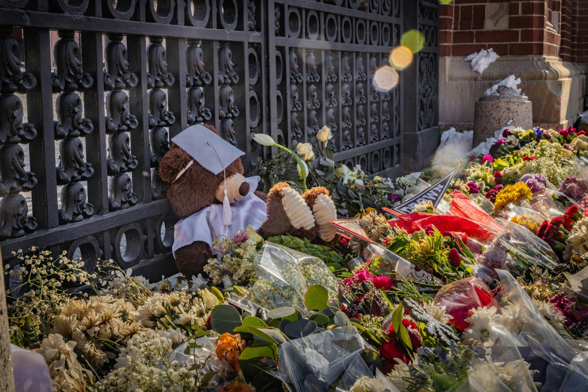 A bear rests on a pile of flowers placed in front of the Van Wickle Gates.