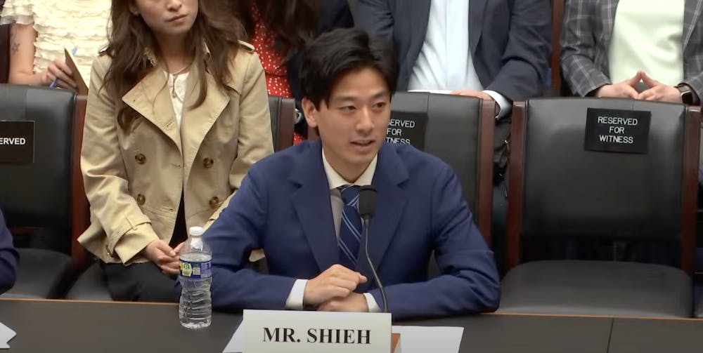 Bloat@Brown creator Alex Shieh ’27 testifying in the congressional hearing Wednesday morning. Shieh is wearing a navy blue suit and sitting in front of a placard labeled "Mr. Shieh."