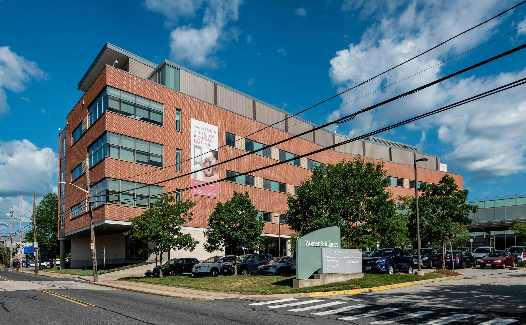 The entrance to the Women and Infants Hospital of Rhode Island. A large sign hangs down the front of the building, which features a picture of a woman and a baby and reads "Women & Infants is a Designated Baby-Friendly USA Hospital." 