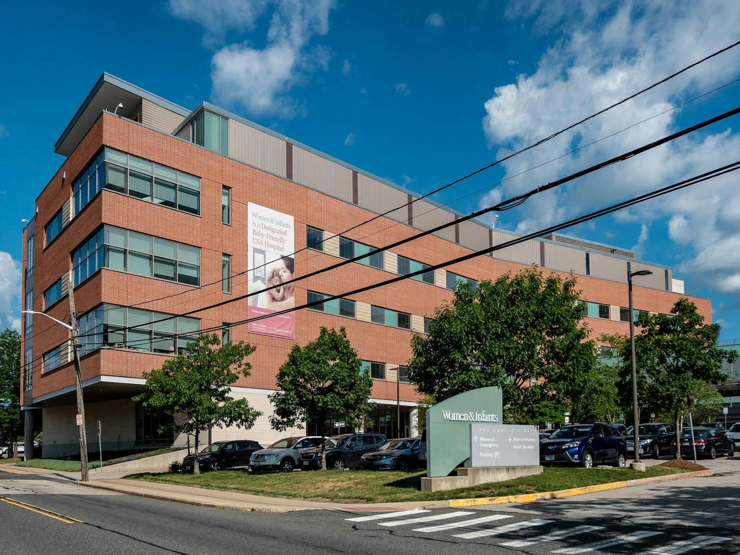 The entrance to the Women and Infants Hospital of Rhode Island. A large sign hangs down the front of the building, which features a picture of a woman and a baby and reads "Women & Infants is a Designated Baby-Friendly USA Hospital."