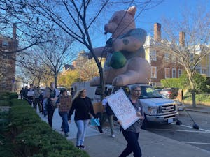 People holding signs reading "Brown violates fair labor practices" in front of Teamsters van that is carrying a large inflatable rat. This is taking place on Waterman Street near Faunce Arch.