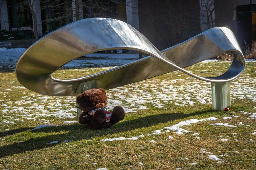A photo of the silver infinity statue outside of Barus and Holley with a teddy bear leaning against it. 