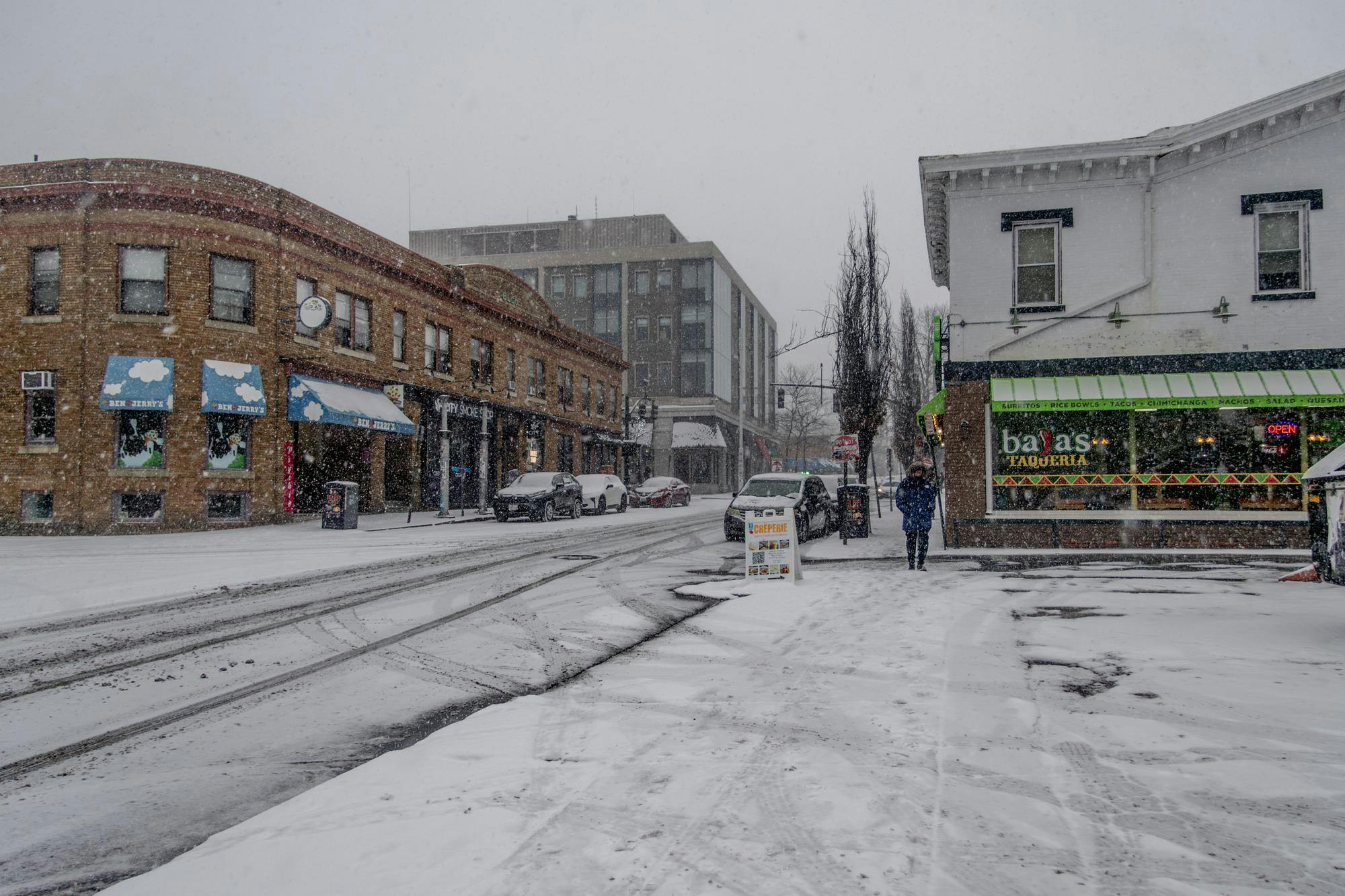 In this photo, a main street with multiple restaurants is covered in snow and mostly empty of people.
