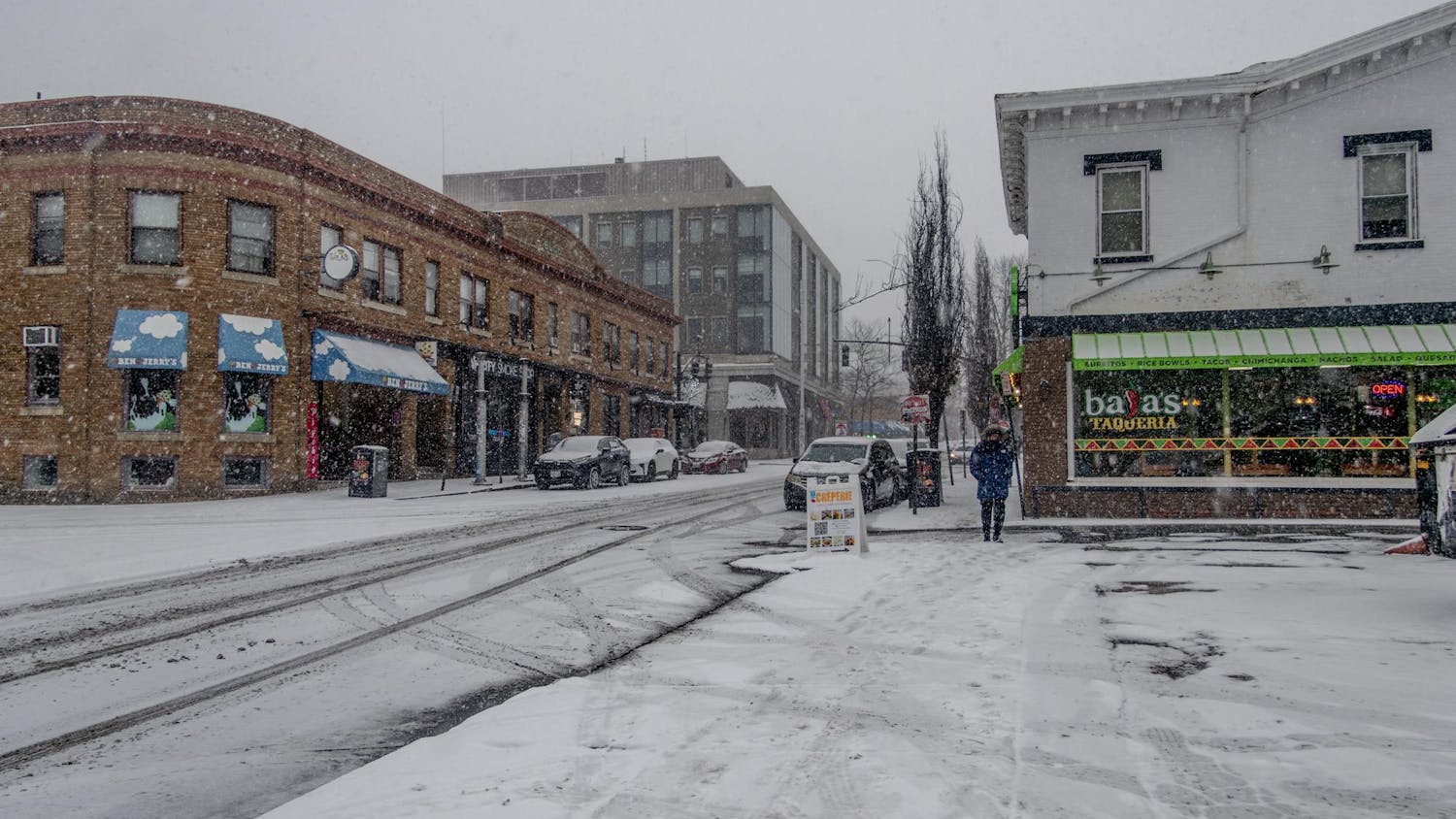 In this photo, a main street with multiple restaurants is covered in snow and mostly empty of people.