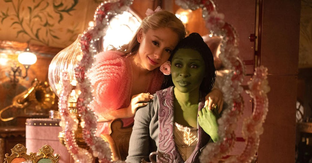 Elphaba Thropp (Cynthia Erivo) and her roommate Galinda Upland (Ariana Grande-Butera) look into the mirror.