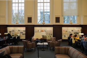 Photo of the "Shared Magma: An American and Swedish Collaboration on Sisterhood and Sister Ore” exhibit at the John Hay Library viewed from across the room, with students working at tables and chairs in front of and to the side of three shadowbox galleries displaying elements of the exhibit.