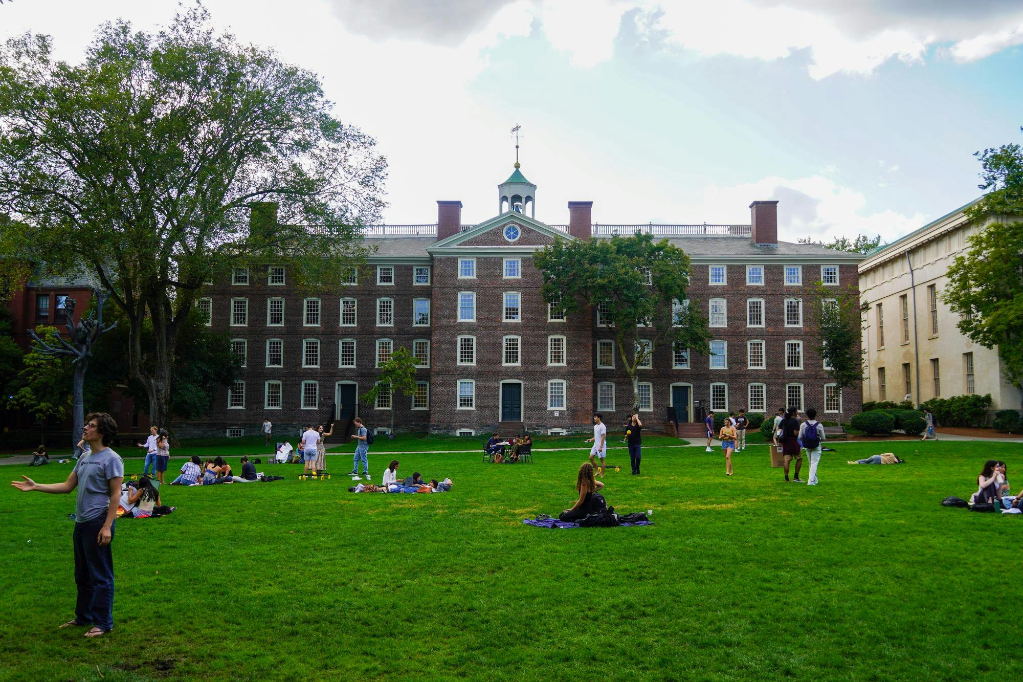 Photo of University Hall with students sitting and talking on the Main Green in front of it.