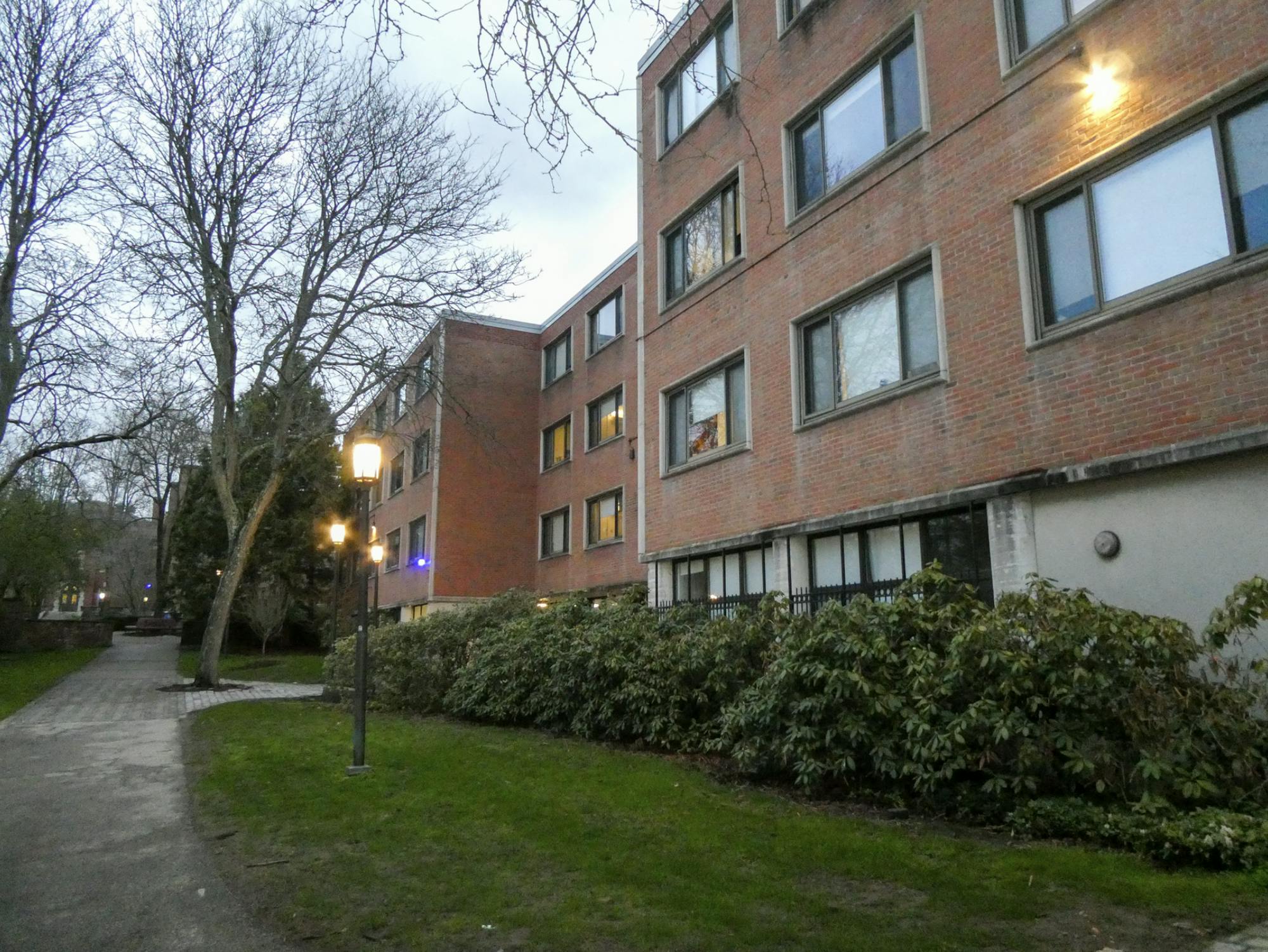 A brick and concrete brutalist building is surrounded by green grass on a rainy, grey day. 
