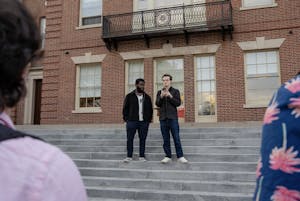 Two men stand on the steps in front of Brown's campus center holding a microphone and a cell phone.