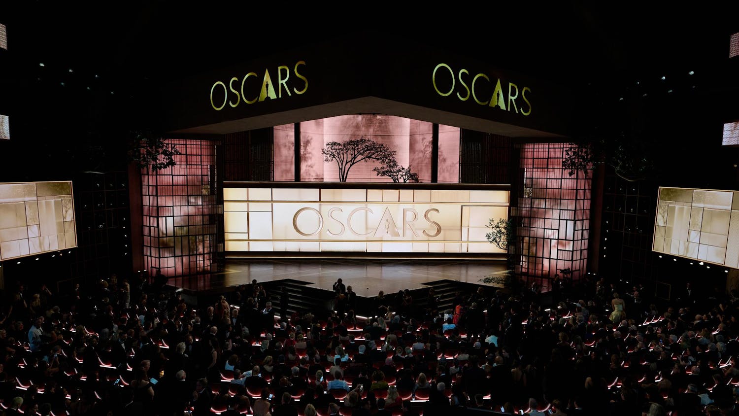 Photo of a dimly lit stage, illuminate by rose-tinted square lights in the background.