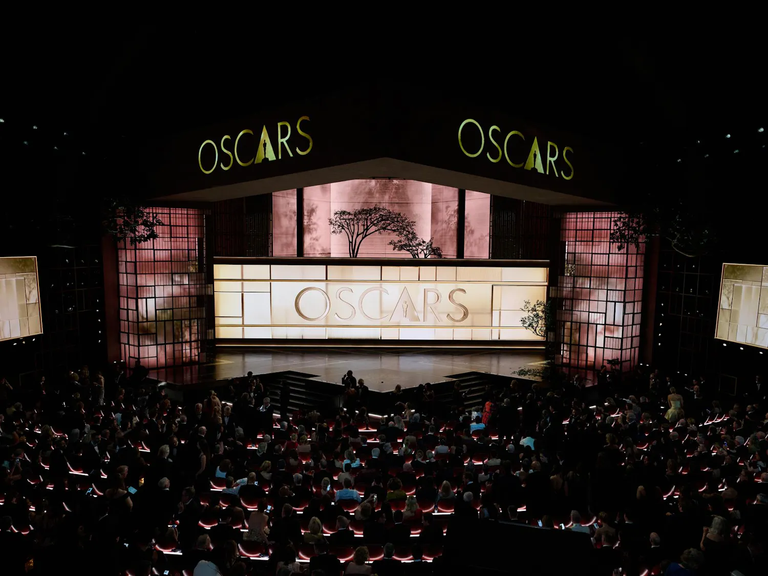 Photo of a dimly lit stage, illuminate by rose-tinted square lights in the background.