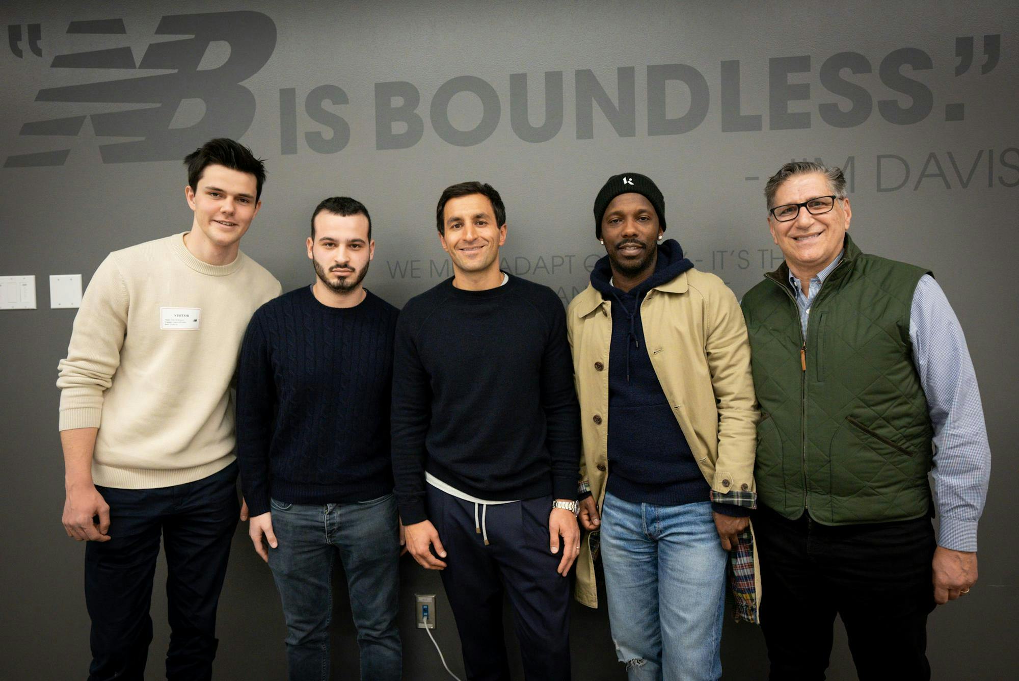 From left to right, the founders of Brown Sports Network, Nikolas Rohrmann and Charlie Pliner, stand beside Chris Davis, New Balance's chief marketing officer, Rich Paul, a sports agent, and Thano Chaltas, a professor at Brown. They are inside a New Balance facility, and the words "New Balance is boundless" are printed on the wall behind them.