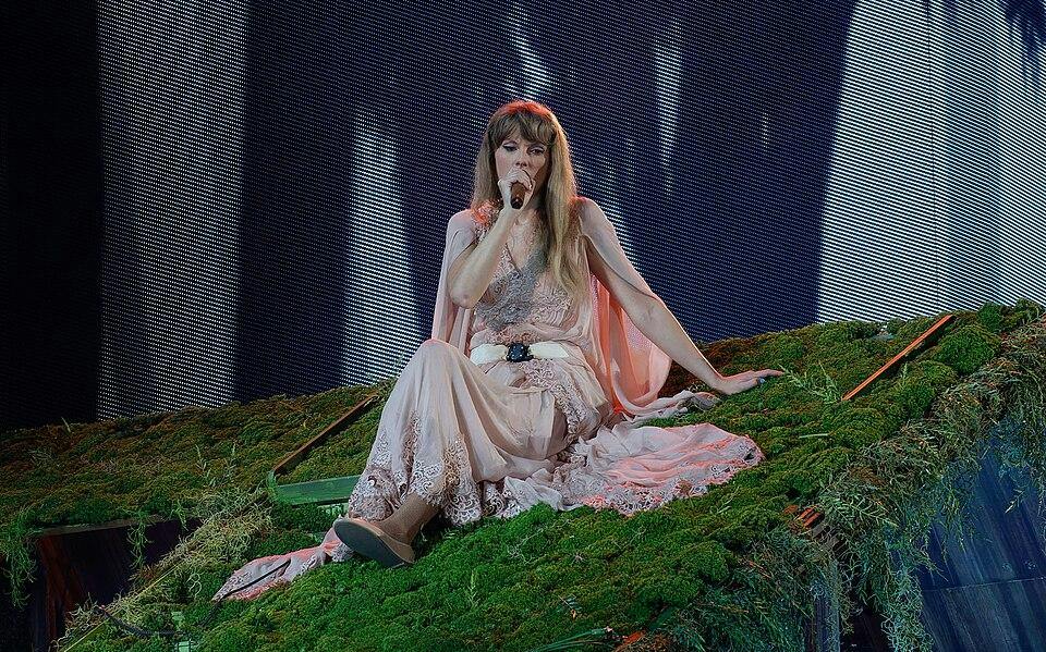An album cover depicts Taylor Swift singing on a slanted faux grass platform.  

