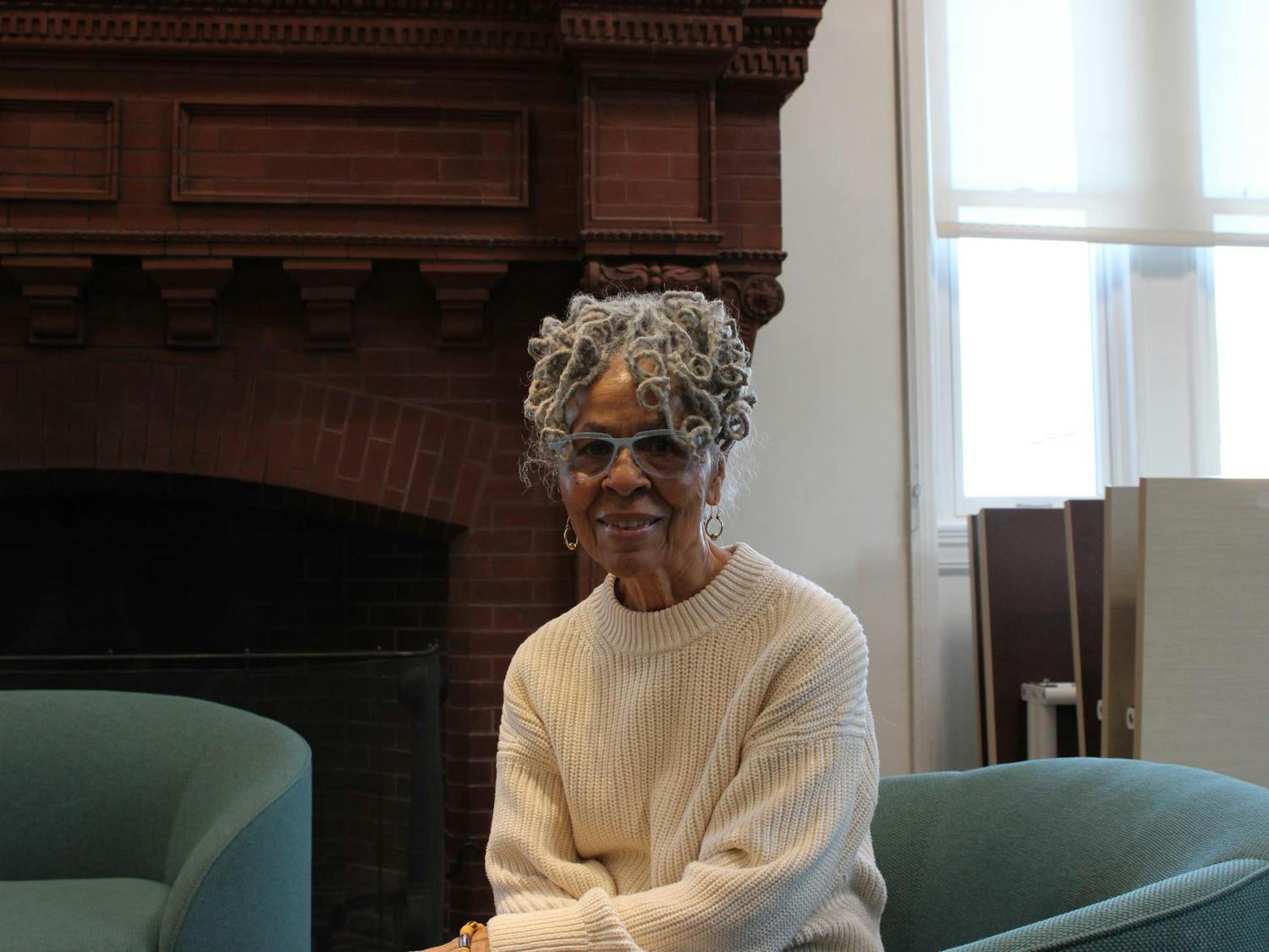 A portrait of Mary Helen Washington. She has gray hair and is wearing a white knitted sweater and blue glasses.