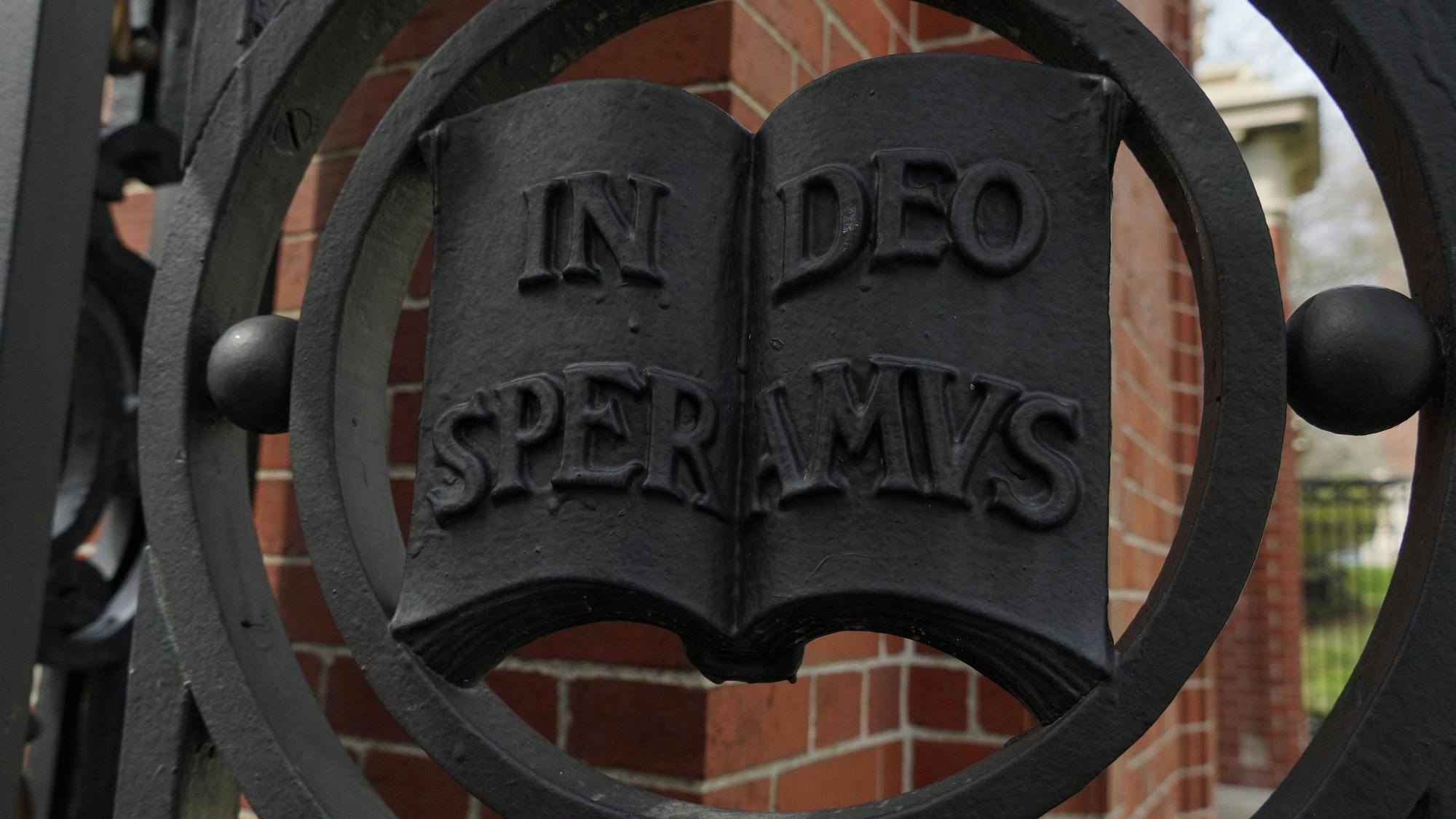 A picture of a metal detailing on the Van Wickle Gates at Brown University. The detailing features an open metal book, with the words In Deo Speramus, Brown's motto.