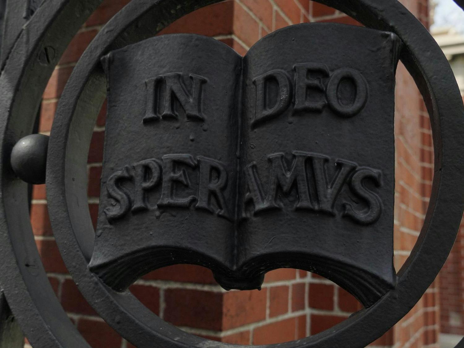 A picture of a metal detailing on the Van Wickle Gates at Brown University. The detailing features an open metal book, with the words In Deo Speramus, Brown's motto.