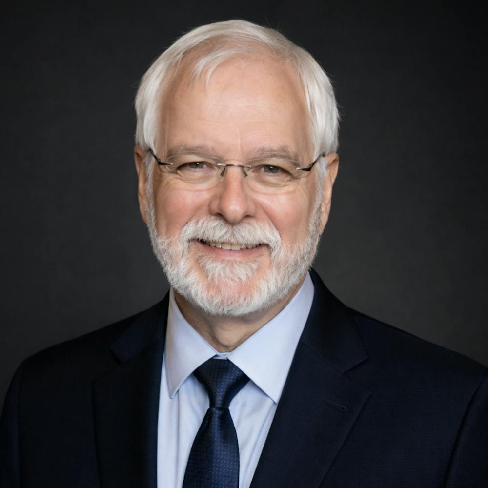 A portrait of John Donoghue PhD’79. An image of an man with white hair and beard, wearing glasses.