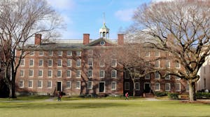 Image of the University Hall with two large bare trees on the left and right sides and multiple students passing by.