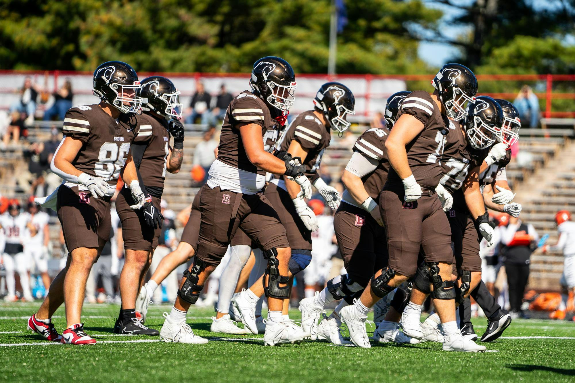 Side shot of Brown football players running across the football field.