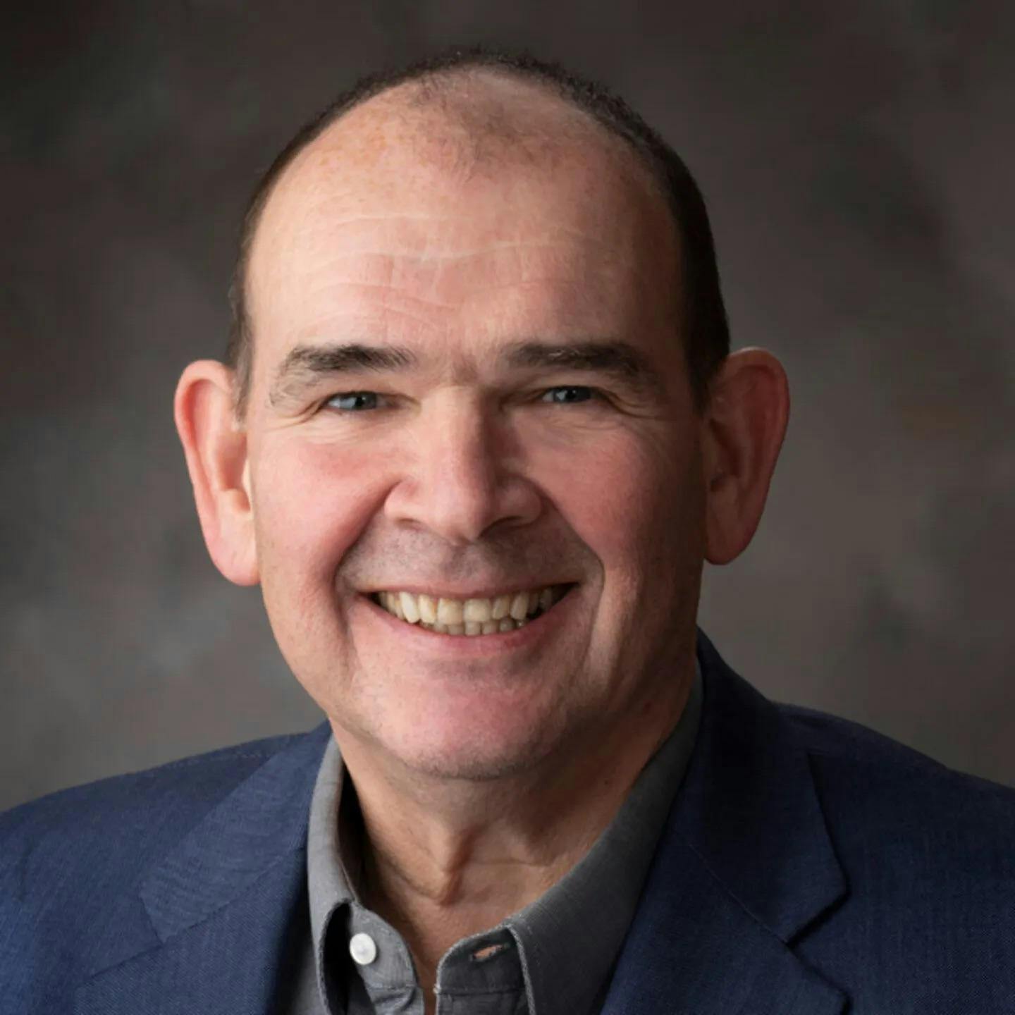Photo headshot of Nicholas Monk smiling wearing a blue blazer.