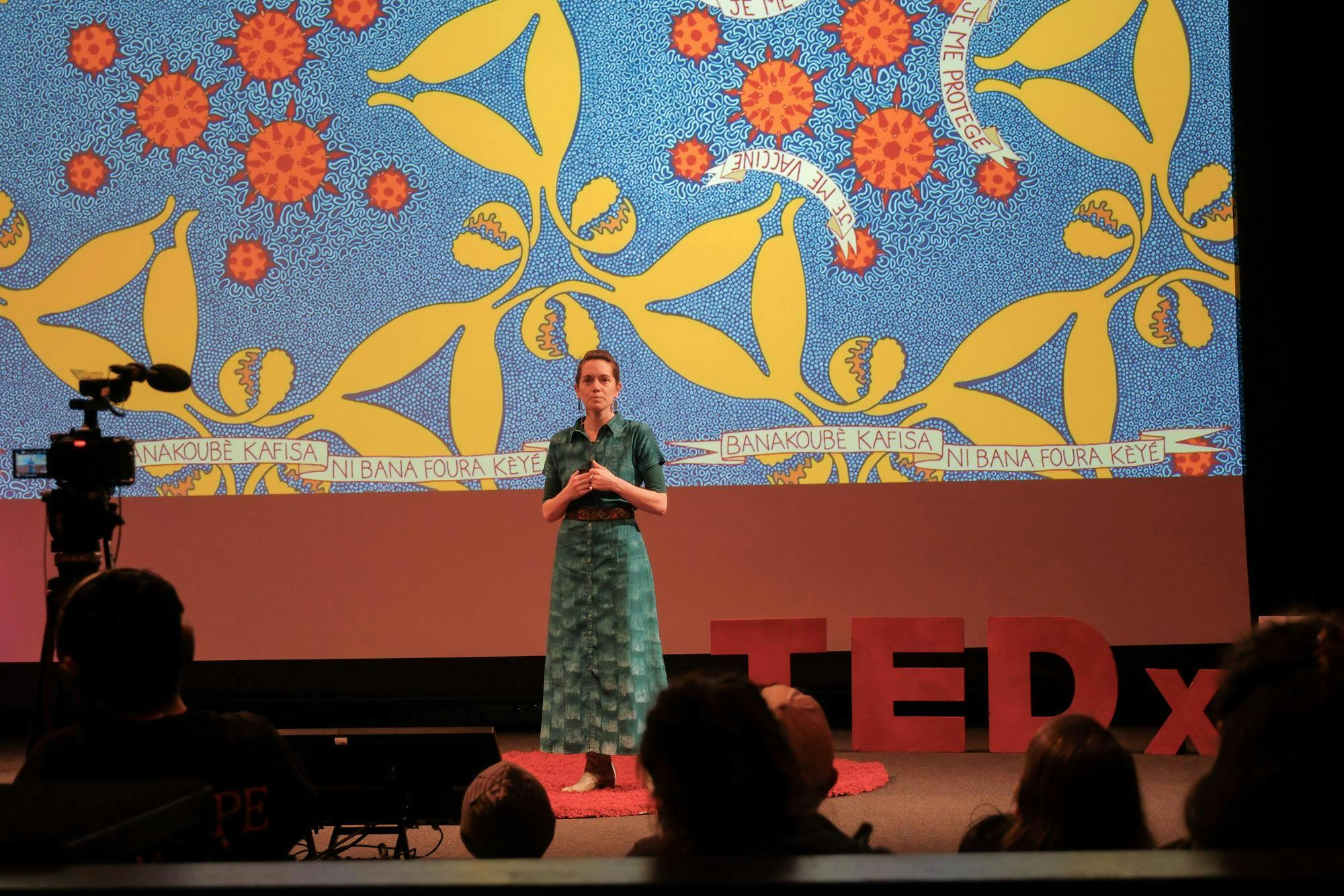 A photo of Eliza Squibb speaking in front of an image of a blue, red and yellow textile.