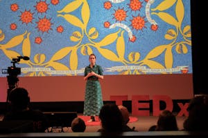 A photo of Eliza Squibb speaking in front of an image of a blue, red and yellow textile.