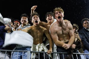 A close photograph of eight men in the stands, caught mid-shout. The three in the center are not wearing shirts, and they are flexing their muscles.  