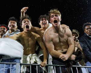 A close photograph of eight men in the stands, caught mid-shout. The three in the center are not wearing shirts, and they are flexing their muscles.