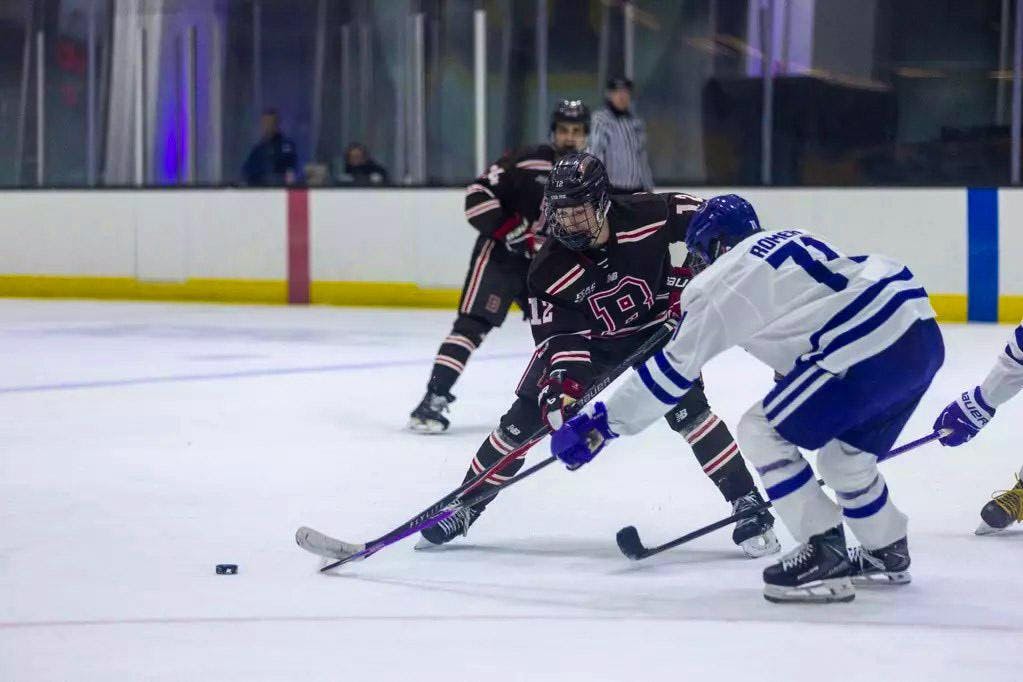 A photo of hockey players on ice reaching for a puck with their hockey sticks. 