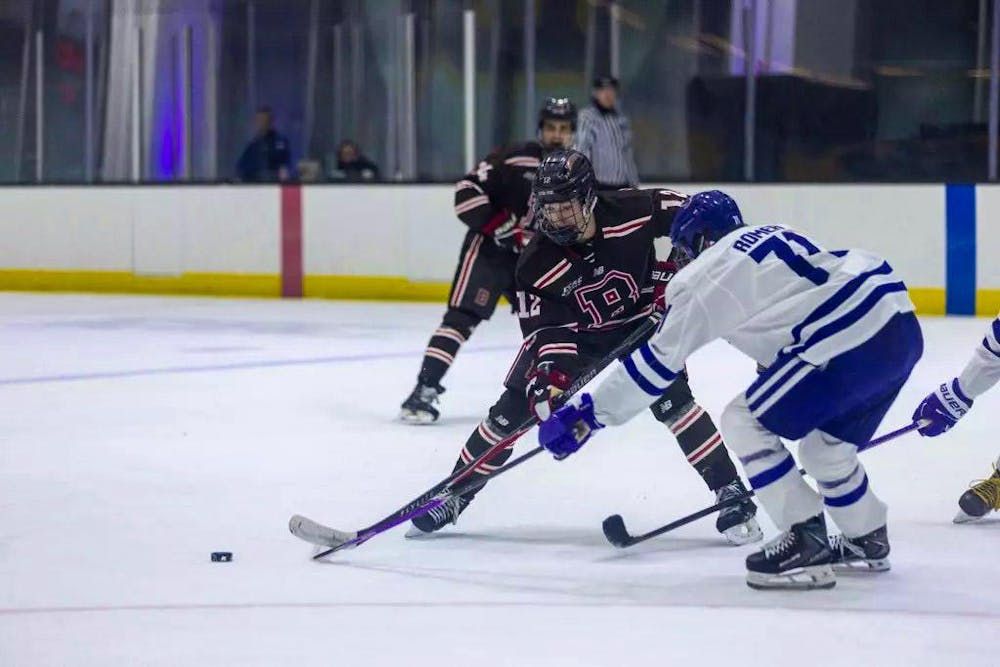 A photo of hockey players on ice reaching for a puck with their hockey sticks. 