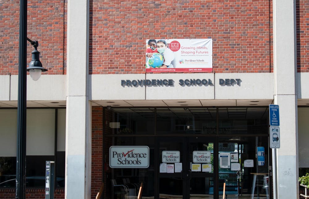 A brick building with a lamppost on the left. The words "Providence School Dept" are in black letters on concrete in the building. The entrance is glass with numerous Providence School stickers on it.