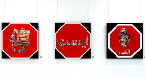 3 stylized  stop signs reading "STOP" in various languages, on a white galllery wall.