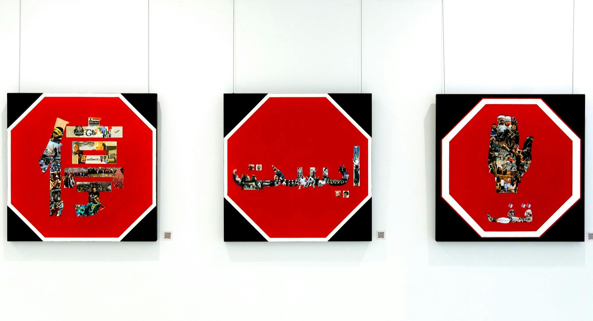3 stylized  stop signs reading "STOP" in various languages, on a white galllery wall.