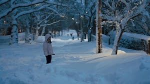A girl in a pink jacket is pictured in knee-high snow, with trees lining the street behind her. 

