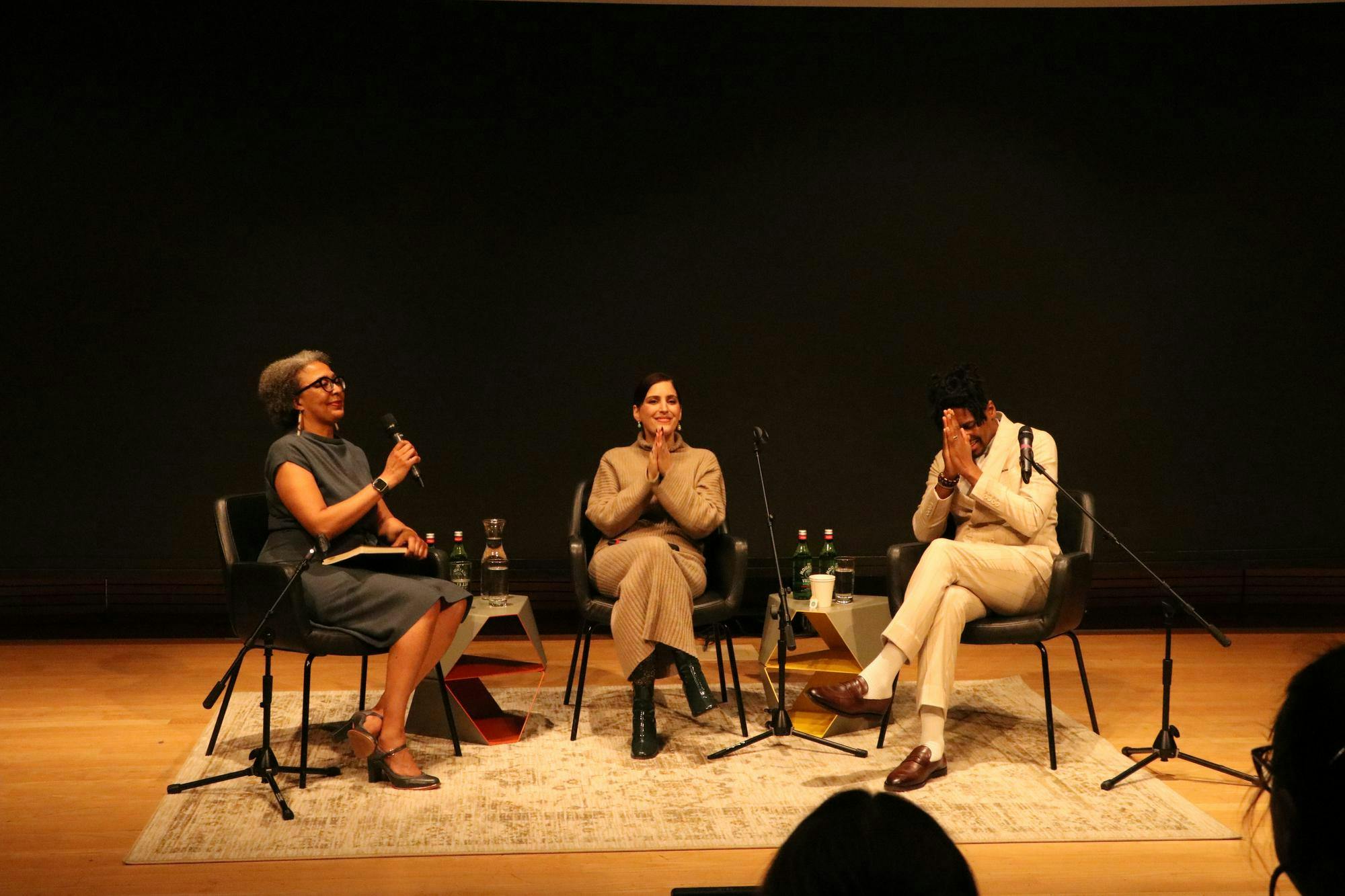 From left to right, Lisa Biggs holds a microphone while Suleika Jaouad and Jon Batiste raise their hands in appreciation.