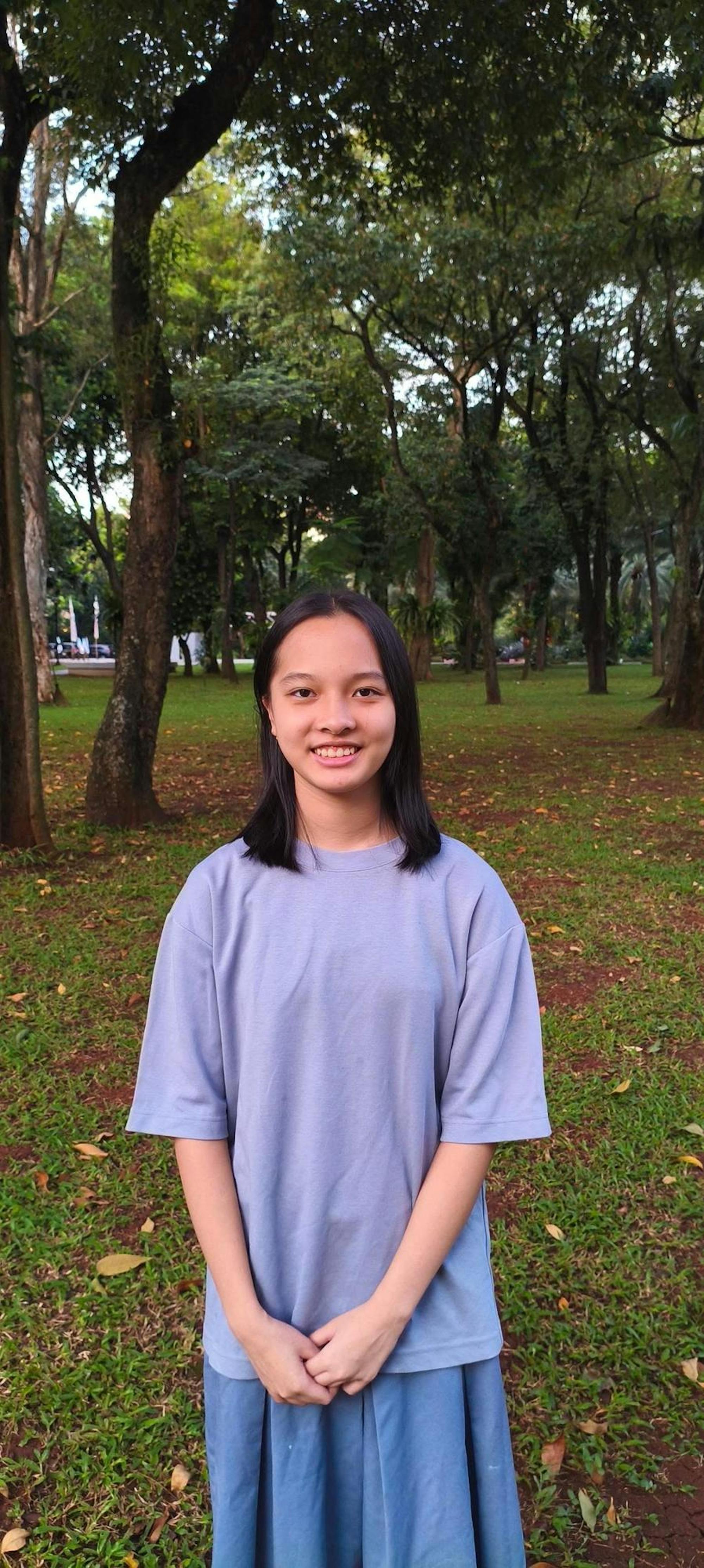 A girl in a purple shirt stands among trees.