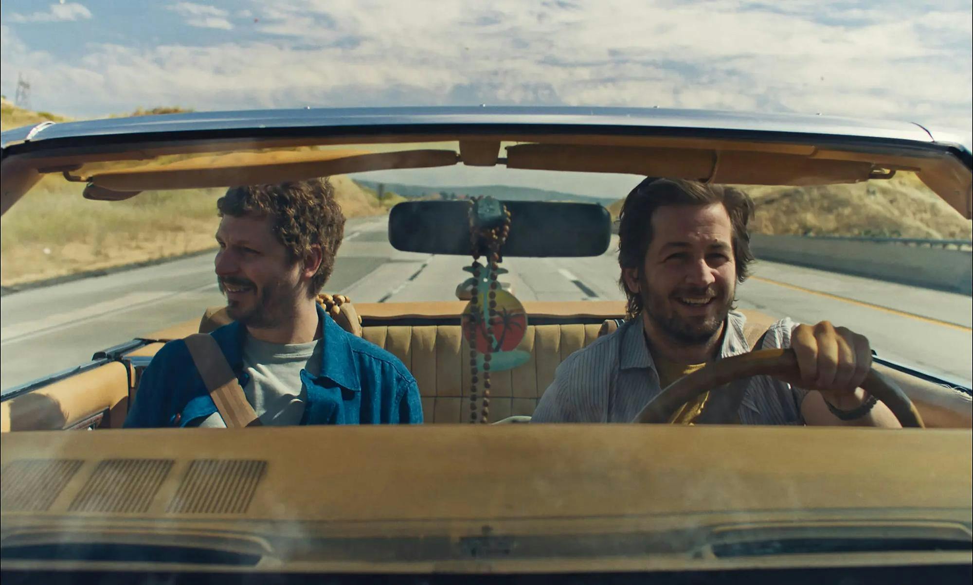 A photo of Michael Cera and Michael Angarano in a car driving down the road. 