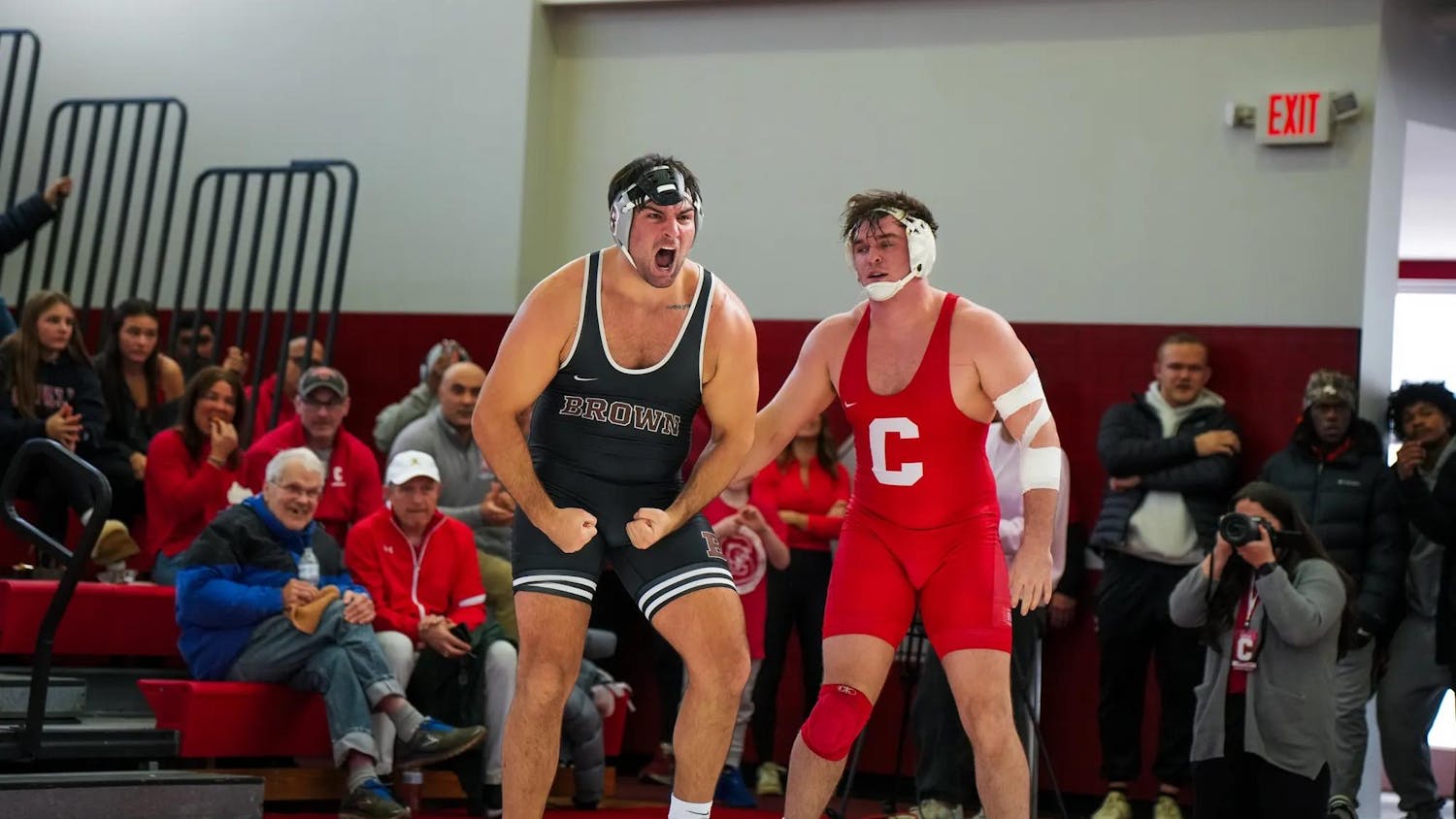 Brown wrestler standing besides Cornell wrestler with a crowd of fans in the background.