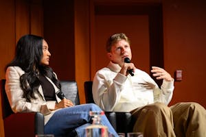 Photo of Hunter Woodhall looking up and gesticulating with his left hand as he speaks into a microphone while Tara Davis-Woodhall looks at him.