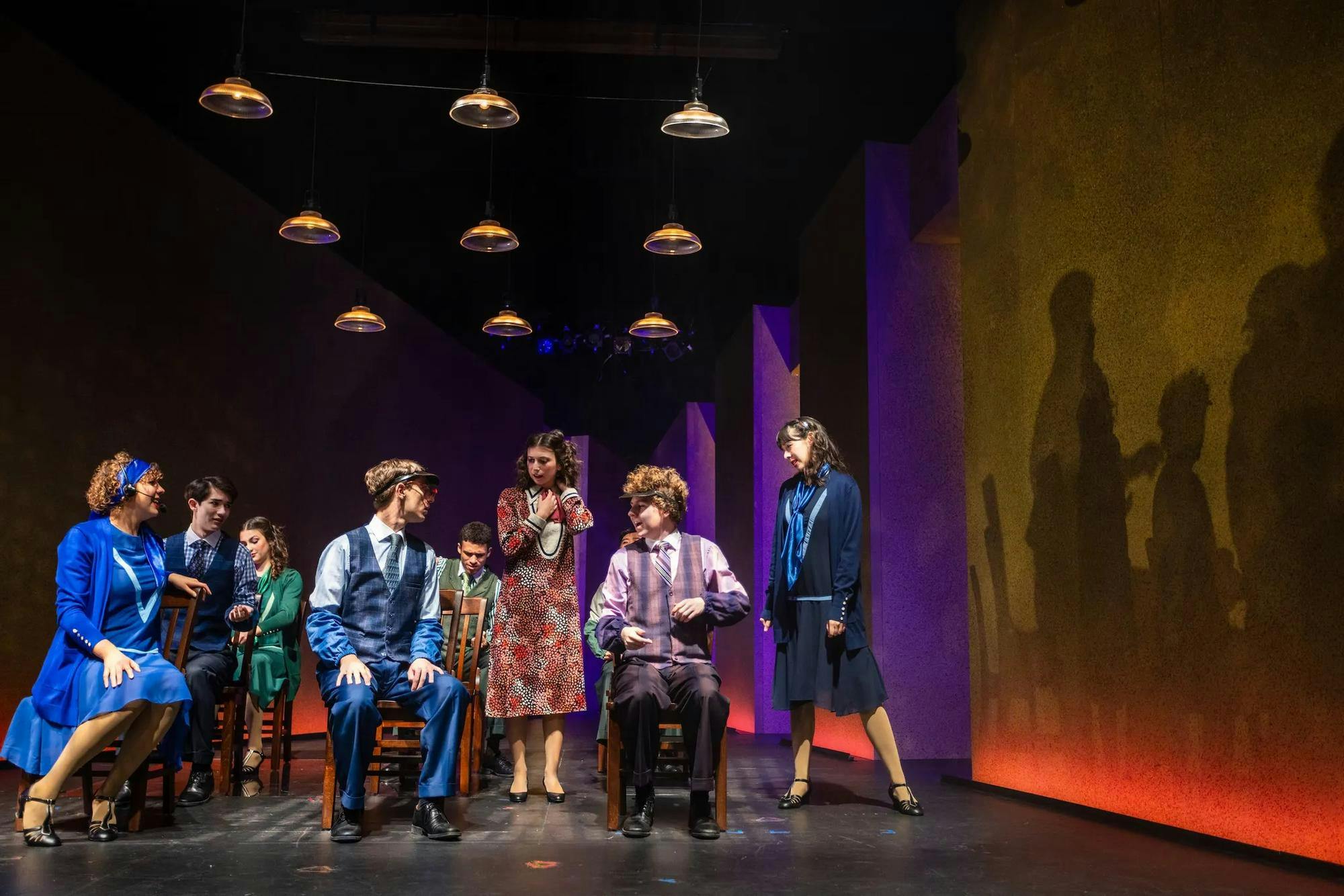 Actors sit on stools on stage