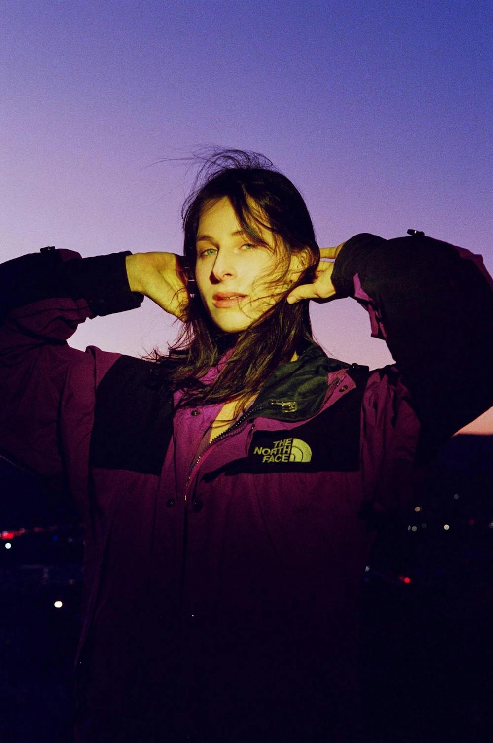 A brunette woman holds her hands on the back of her head in a film photo. 