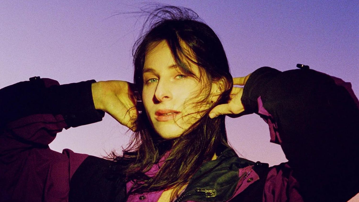 A brunette woman holds her hands on the back of her head in a film photo.