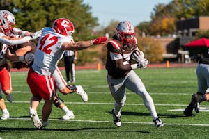 A photo of a Brown player running with the ball as Cornell players try to stop him.

