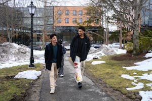 Lewis talks to another man as they walk through a park. There is snow and green grass behind them.