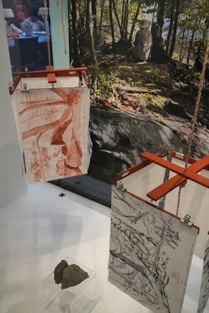 Photo of Kajsa Eriksson’s “Huggen, Hugga, Huggas [Cut, Cut, Cut],” which features two hanging mobile made of four hanging watercolor paintings arranged squarely around a central wooden crossbeam.