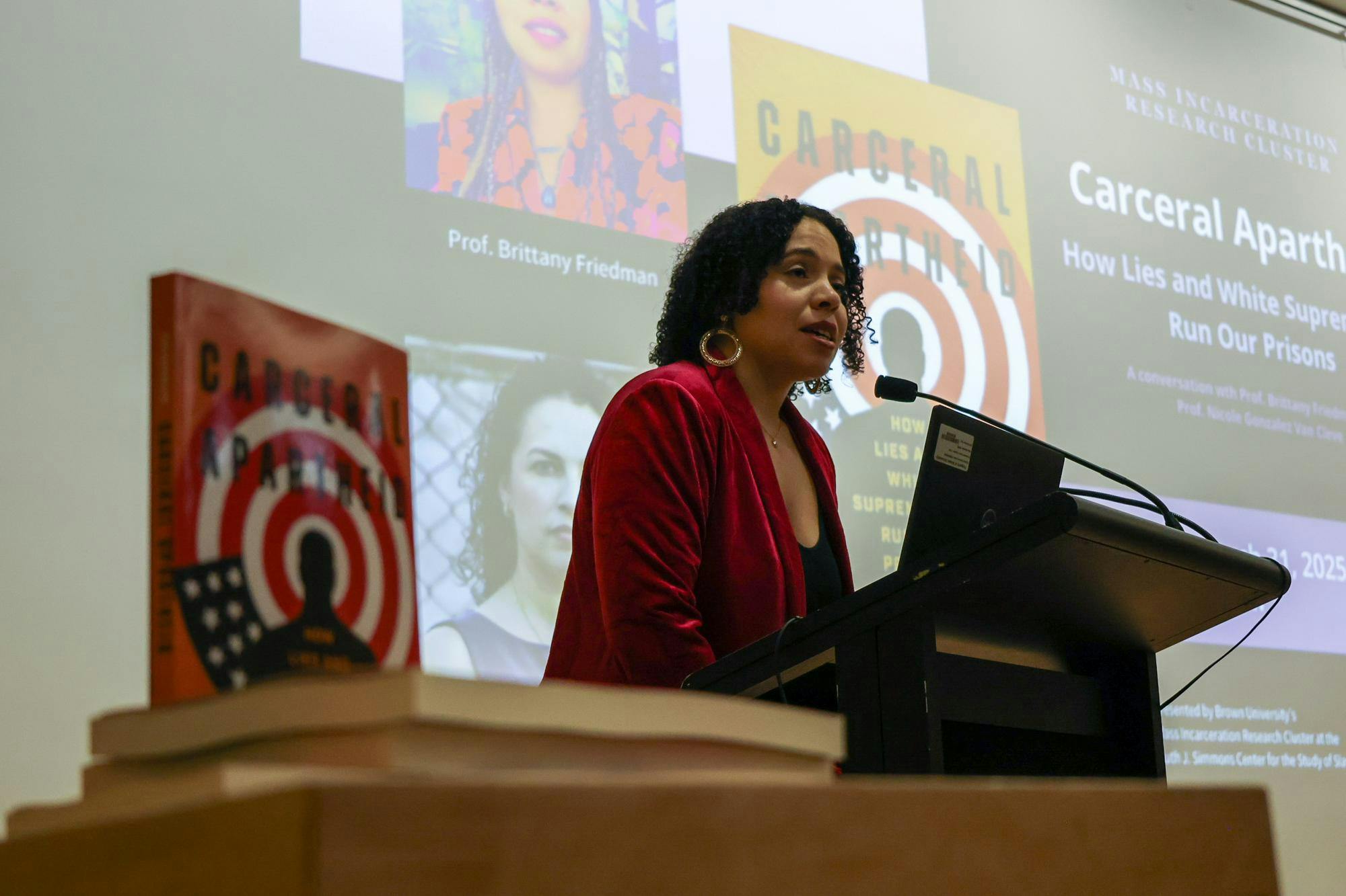 A picture of Brittany Friedman speaking at the Monday morning event. A copy of the book "Carceral Apartheid" is in the foreground.