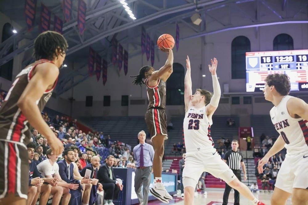 Four men playing basketball. One man jumps and motions to shoot the ball while an opposing player tries to block him. 