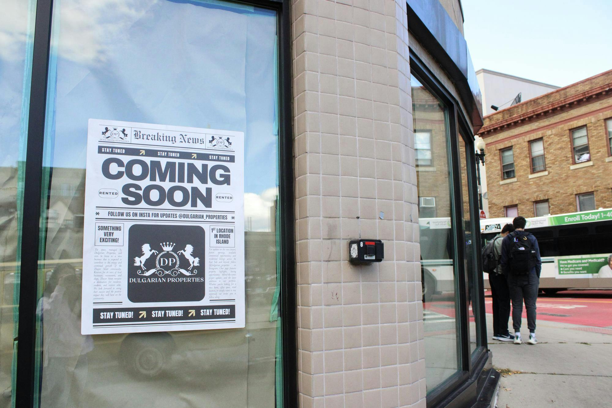 Photo of the rounded corner of a tan tile building with its windows covered with brown paper and a poster that shows the two-horse Dulgarian Properties logo and reads “Coming Soon”. 