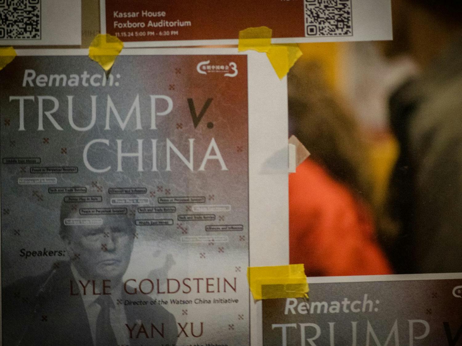 The image focuses on a poster advertising the panel, and features Donald Trump's face as well as the words "Rematch: Trump v China." The edges of a few other taped-up posters are also visible.