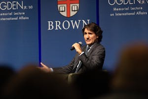 Justin Trudeau speaking into a microphone against a blue Brown University-branded backdrop.